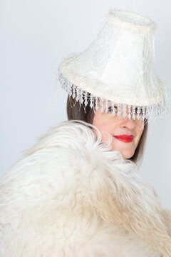 Mature woman wearing fur with lamp shade on head against white background