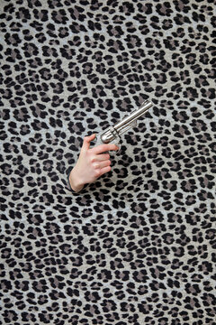 Studio shot of female hand holding old-fashioned revolver through leopard print pattern