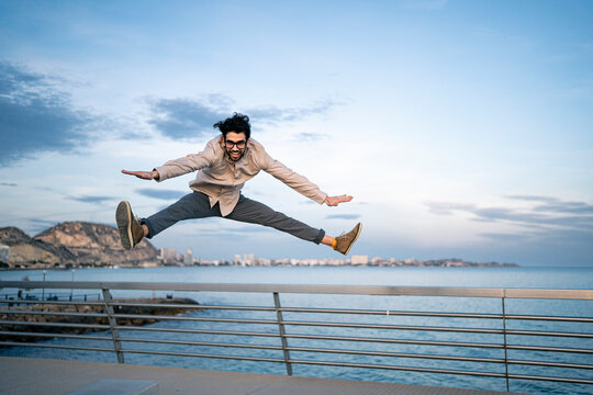 Male business professional with arms outstretched doing splits in mid-air in front of blue sky
