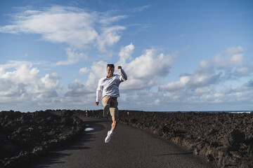 Cheerful male tourist jumping amidst volcanic rock at Los Hervideros on sunny day, Lanzarote, Spain