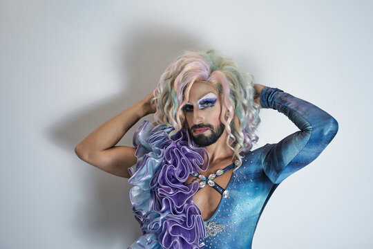 Drag queen with hand in hair standing against white wall