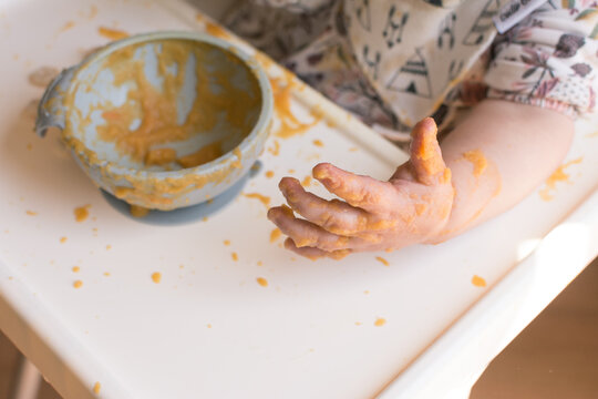 Self feeding: young baby making a mess eating puree with hands following bay led weaning
