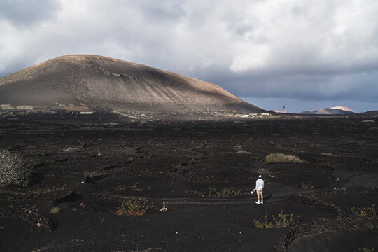 Young male tourist standing on black soil in vineyard at El Cuervo Volcano during vacations, Lanzarote, Spain