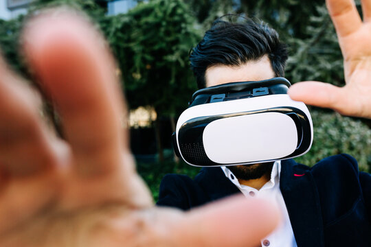 Businessman wearing virtual reality headset stretching hand while standing outdoors