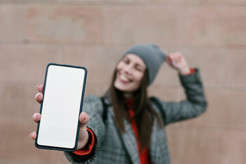 Woman showing blank smart phone screen against wall