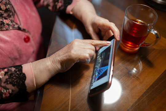 Senior woman touching screen of mobile phone on table at home