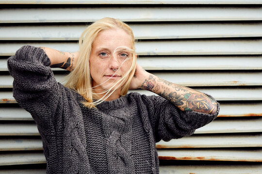 Tattooed woman with hand in hair standing in front of shutter