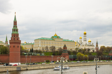 Moscow / Russia - May, 5, 2021: view of the brick wall, the yellow Grand Kremlin Palace and the Assumption Cathedral with golden domes on the banks of the Moskva River on a cloudy spring day
