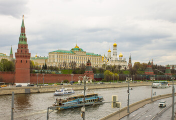 Fototapeta premium Moscow / Russia - May, 5, 2021: view of the brick wall, the yellow Grand Kremlin Palace and the Assumption Cathedral with golden domes on the banks of the Moskva River on a cloudy spring day