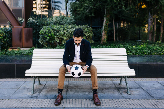 Mid adult businessman holding soccer ball while sitting on bench
