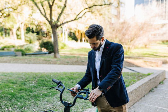 Businessman using mobile phone while standing by bicycle at park