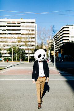 Businessman wearing panda mask walking on footpath in city