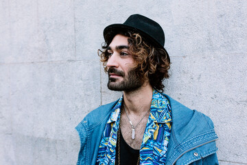 Young man with hat looking sideways in front of wall
