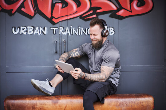 Smiling male athlete using digital tablet outside gym against graffiti door
