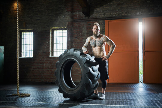 Male athlete with hand on hip standing by tire in sports studio