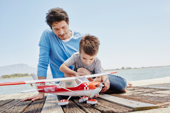 Boy checking toy airplane while sitting on pier