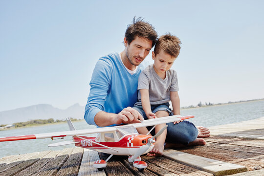 Mature man and boy talking while touching toy airplane on pier
