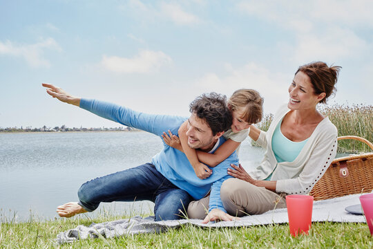 Daughter and father having fun while sitting by mother on blanket by lake