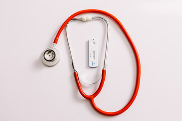Rapid covid-19 antigen test with positive result next to stethoscope on white background....