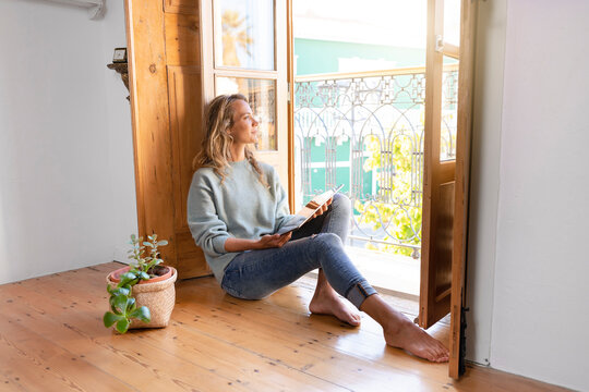 Thoughtful woman with digital tablet looking out of window at home