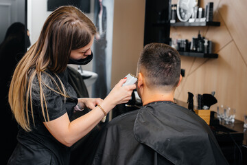 Fototapeta premium A professional stylist in a modern stylish barbershop shaves and cuts a young man's hair. Beauty salon, hair salon