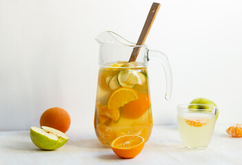 Fruit healthy lemonade with fresh orange, cucumber, tangerine, lemon, apple and honey in glass jar with wooden spoon on white background