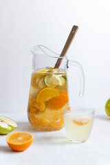 Fruit lemonade with fresh orange, cucumber, tangerine, lemon, apple and honey in glass jug with wooden spoon on white background