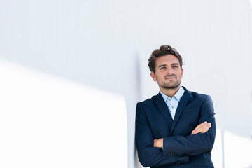 Mid adult businessman looking away while standing with arms crossed on wall