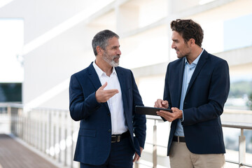 Business people discussing over digital tablet while standing at office building terrace