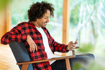 Smiling man using smart phone while sitting on armchair by window