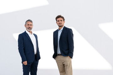 Mature businessman with colleague staring while standing against white wall