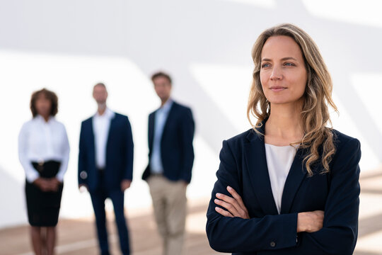 Female entrepreneur looking away while standing with colleagues in background at office terrace