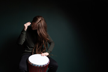 Percussion musician. Pretty young woman playing djembe. Green background.