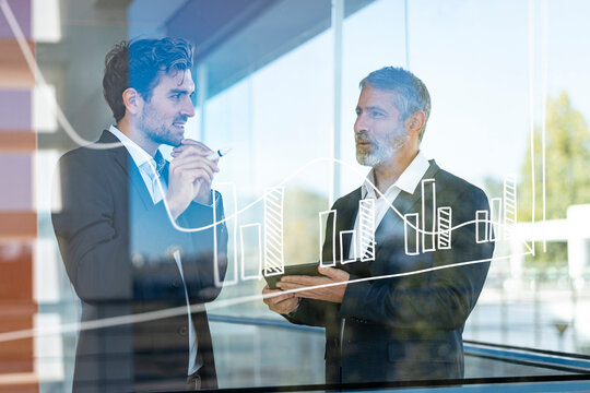 Businessmen discussing over graph while standing in modern office