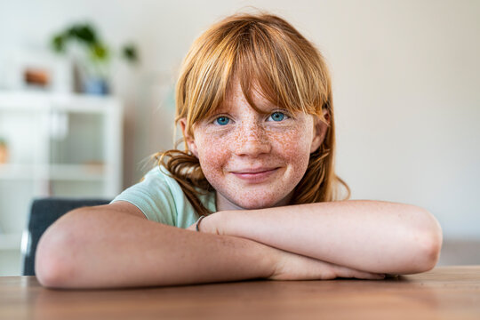 Smiling girl with arms crossed sitting at table in living room