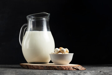 Central asian traditional kurut cheese in a white plate with a jug of fresh milk on a wooden board in low key