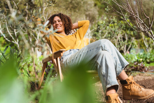 Smiling woman looking away while relaxing on chair during springtime in vegetable garden