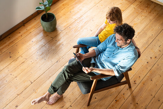 Father and daughter looking at digital tablet while sitting on armchair