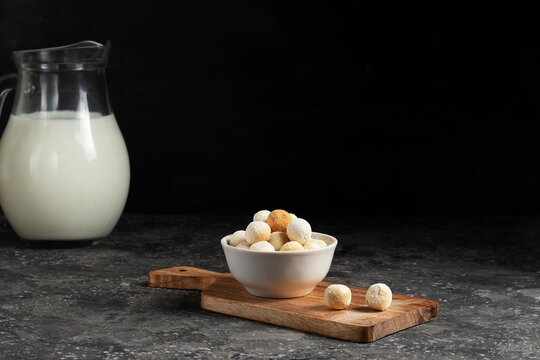 Central asian traditional cheese kurut in a white plate with a jug of fresh milk on a wooden board on a dark background