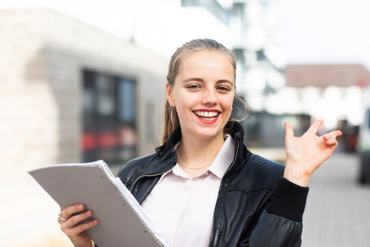 Portrait of young blonde woman standing outdoors with note pad in hand