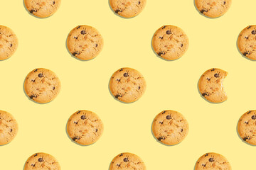 Seamless pattern of whole and bitten American cookies with chocolate pieces on yellow background