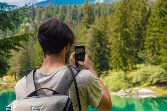 Male hiker taking photo of Cauma Lake through mobile phone while standing at Graubunden Canton, Switzerland
