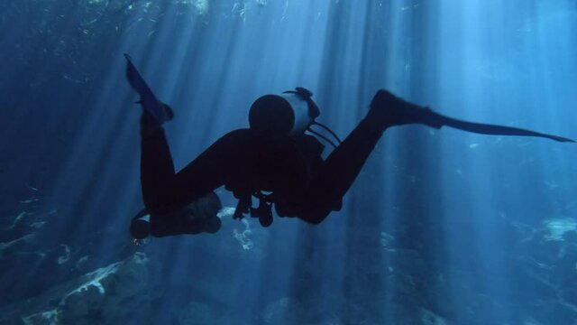 Divers swimming in a cenote with light rays. Divers in a cave. Clear water diving. Elden Cenote