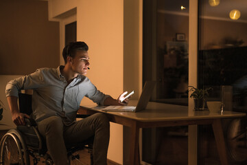 Disabled male business professional with laptop wearing headphones while sitting on wheelchair in living room
