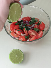 hand squeezes lime juice into tomato and green salad
