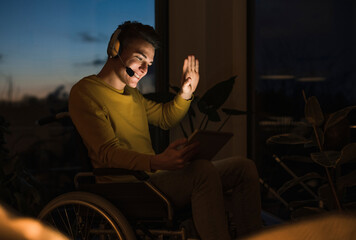 Smiling young man in wheelchair gesturing while making video call through digital tablet sitting on wheelchair in living room