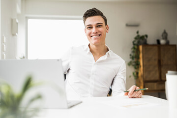 Smiling young man with laptop sitting at desk