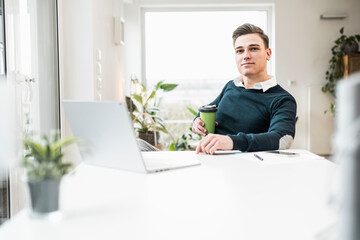 Businessman with disposable coffee cup sitting at home office