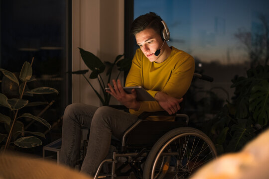 Disabled young man using digital tablet while sitting on wheelchair in living room