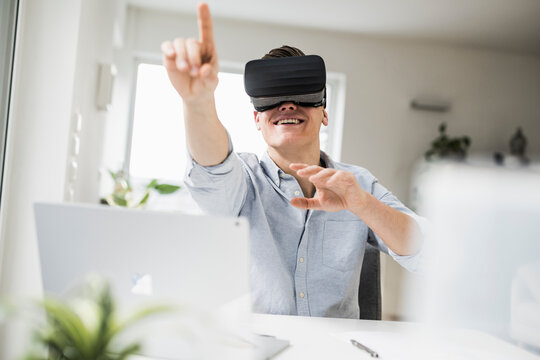 Smiling male professional wearing virtual reality simulator gesturing while sitting in home office